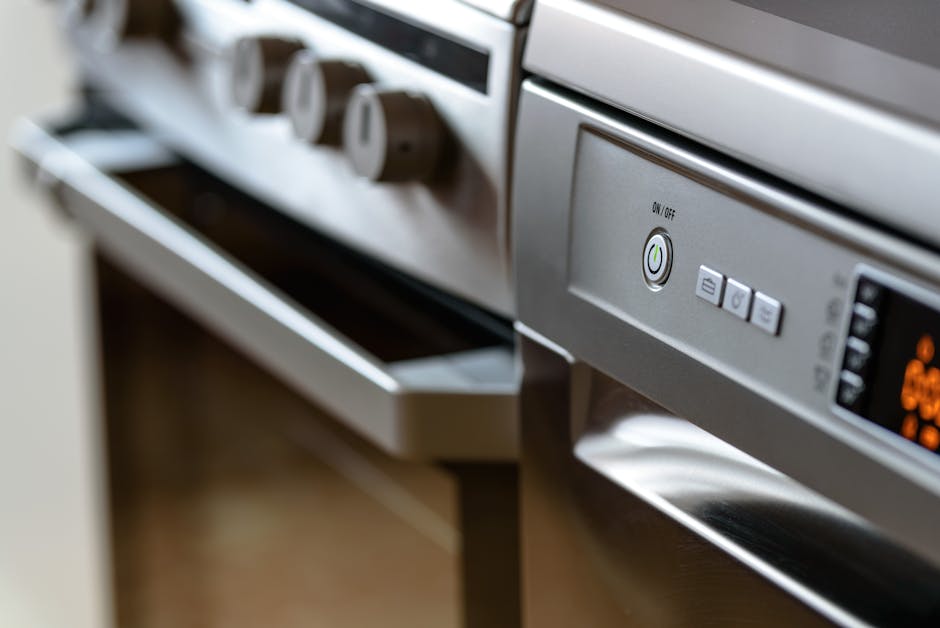 A modern kitchen featuring a white countertop with an integrated black electric induction cooktop. In the background, there are built-in double ovens with stainless steel finishes, set into a white ca